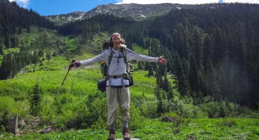 a backpacker spreads their arms out wide with a green mountain landscape in the background